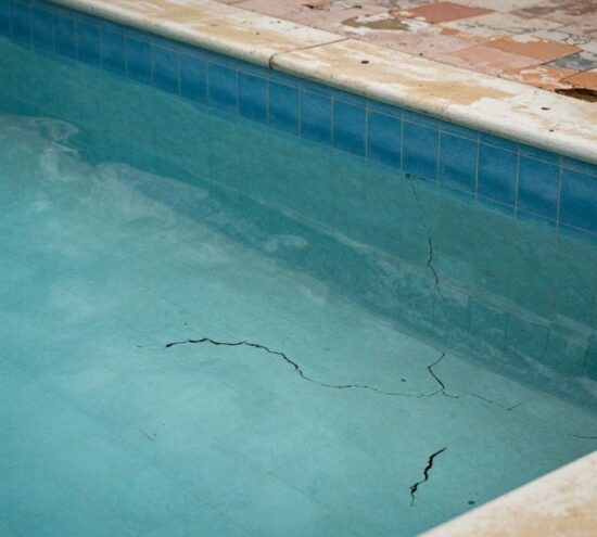 Piscine vieillissante avec fissures et revêtement décoloré.