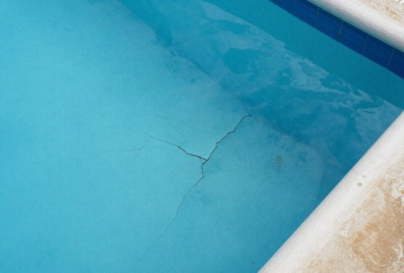 Piscine coque fissurée et décolorée avec terrasse usée.